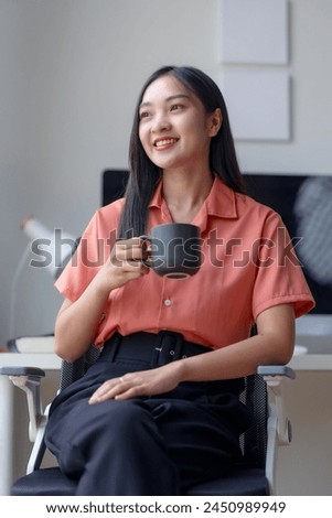 Smiling professional asian woman enjoying a coffee break at the office. Casual business portrait with natural light. Work-life balance and office culture concept