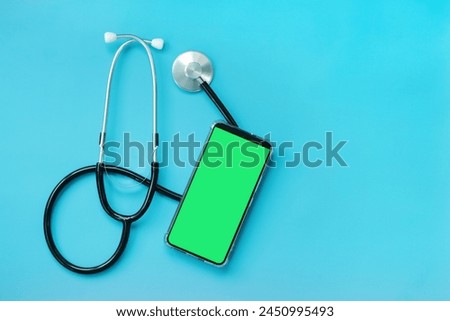Stethoscope on a blue background and a smartphone with a green screen, top view. Cardiology and healthcare concept. Auscultation device. Chromatic mobile phone mockup. Online medical help concept