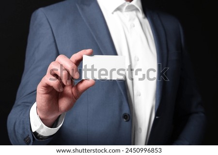 Businessman holding blank business card on black background, closeup
