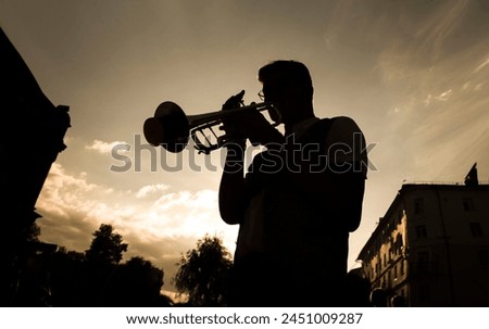 silhouette of a street musician playing the trumpet against the backdrop of the sunset sky Royalty-Free Stock Photo #2451009287