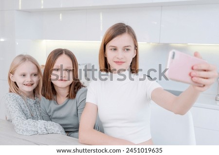 girl is taking picture her two younger sisters. The girls are smiling and seem to be enjoying the moment. The photo captures a happy and loving family moment
