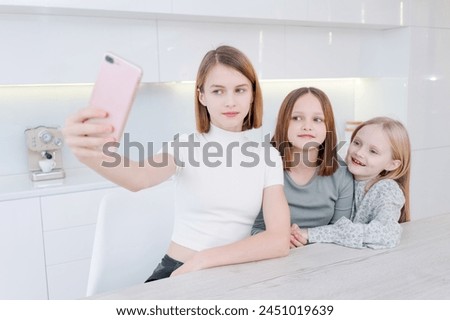 girl is taking picture her two younger sisters. The girls are smiling and seem to be enjoying the moment. The photo captures a happy family moment