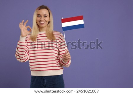 Happy young woman with flag of France showing OK gesture on purple background