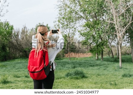 Hiker with his back turned to take out his phone to take photos during a field trip Royalty-Free Stock Photo #2451034977