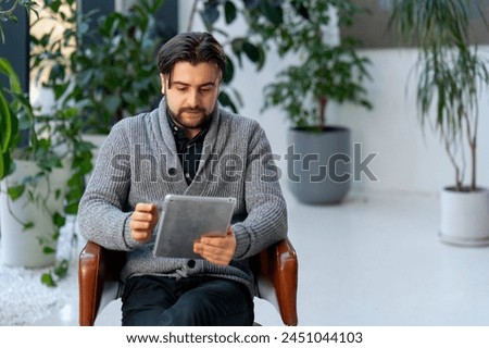 in a white hall a young guy office worker on a brown chair working with a tablet