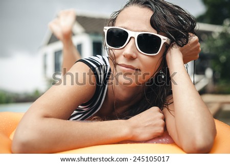 Close-up of young woman lying on an inflatable mattress near the pool. Cute girl in sunglasses resting wet from rain