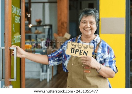 Asian Elderly Smiling women, Senior woman exudes warmth, business owner positions the open sign at the coffee shop entrance. happiness of opening coffee shop in morning small family business