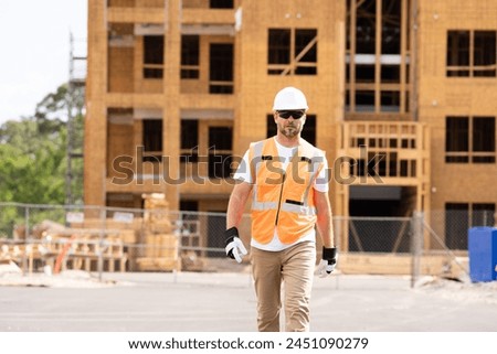 roofer builder working on roog structure of building on construction site. handsome young male builder in hard hat smiling at camera. Construction Worker on Duty. Contractor and the Wooden House Frame Royalty-Free Stock Photo #2451090279