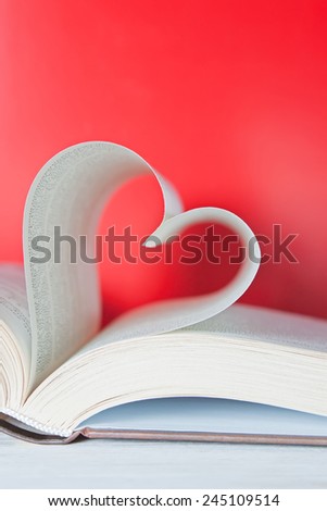 pages of a book curved into a heart shape on red background.