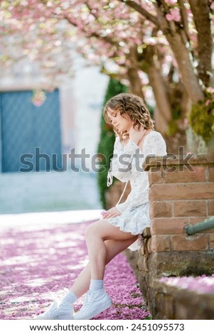 Beautiful young blonde in light romantic dress. Portrait of young woman near blooming sakura tree in a European city. Spring.
