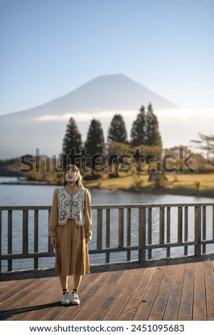 Experience the joy of a vacation: Asian woman in a casual dress takes in the stunning scenery of Mount Fuji, capturing sunny morning and the serene beauty of Kawaguchiko Lake.