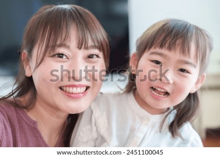 portrait of young asian mother and daughter taking selfie looking into the camera