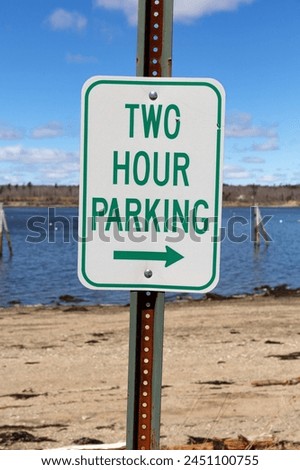Vertical composition of a two hour parking sign with a right arrow in the foreground with a view of Stockton Harbor in Maine in the background.