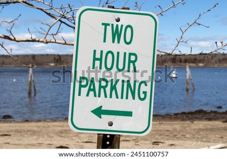 Two hour parking sign with a left arrow at an angle in the foreground with a view of Stockton Harbor in Maine in the background.