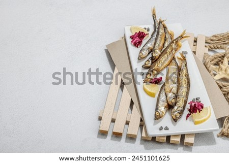 Smoked smelt with fresh lemon and herbs. Salted fish with marine decor. Trendy pallet, sea rope. Hard light, dark shadow, light stone concrete background, copy space Royalty-Free Stock Photo #2451101625