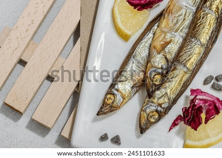 Smoked smelt with fresh lemon and herbs. Salted fish with marine decor. Trendy pallet, sea rope. Hard light, dark shadow, light stone concrete background, top view Royalty-Free Stock Photo #2451101633