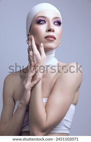 Exploring modern beauty trends. Young woman, with purple eyeshadow makeup, hand on cheek, posing on pastel purple background. Concept of beauty, fashion, cosmetics and cosmetology, style Royalty-Free Stock Photo #2451102071