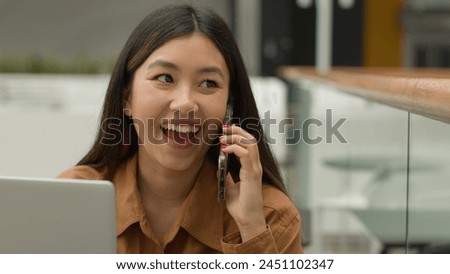 Smiling Asian woman businesswoman working online with laptop in office chinese japanese girl student freelancer talk mobile phone laughing excited female answer smartphone call carefree conversation Royalty-Free Stock Photo #2451102347