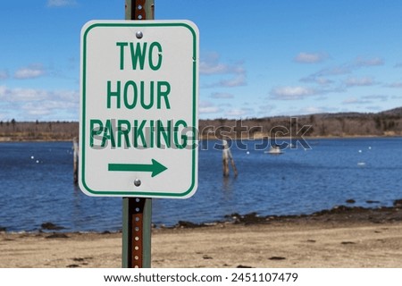 Two hour parking sign with a right arrow in the foreground with a view of Stockton Harbor in Maine in the background.