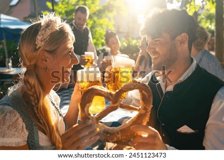 Couple in traditional German attire or tracht, holding beer mugs and pretzel, enjoying Oktoberfest outdoors Royalty-Free Stock Photo #2451123473