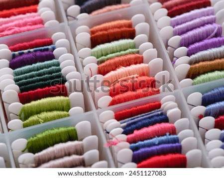 A lot of plastic bobbins with different colour embroidery threads in a plastic sorting box. Royalty-Free Stock Photo #2451127083