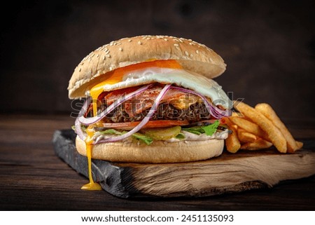 Burger with beef patty, bacon, cheese and egg. Juicy delicious hamburger on darkmood picture for restaurant decoration, poster. 