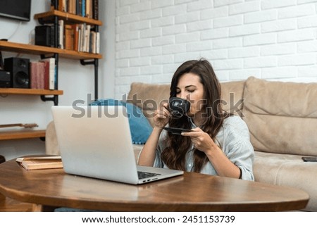 Young freelance business woman graphic designer taking a break from working at home and talk on video call with friend while drinking tea or coffee and enjoying in conversation.