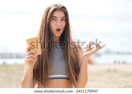 Young pretty caucasian woman holding a take away coffee at outdoors surprised and pointing side