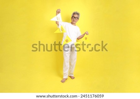 Senior man in white color with gesture of holding Chinese vegetarian festival flag isolated on yellow background. J festival, Translation for Chinese and Thai text is refrain eating meat.