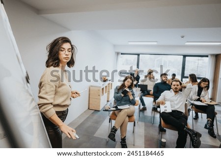 Engaged female leader with glasses presenting at a business workshop, with attentive colleagues in a well-lit, contemporary office setting. Royalty-Free Stock Photo #2451184465