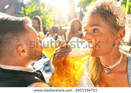 Woman an Man in Tracht drinking a mass of beer surrounded by her friends at beer garden or oktoberfest Royalty-Free Stock Photo #2451194751