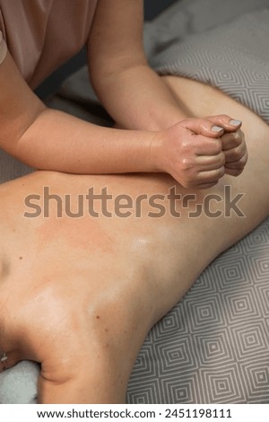 Caucasian woman undergoing manual oil massage of her back. Vertical photo.