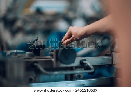 Close up of graphic technician's hand adjusting and manipulating silkscreen printing machine at printing shop. Cropped picture of unrecognizable graphic expert's hands operating screen printing press.