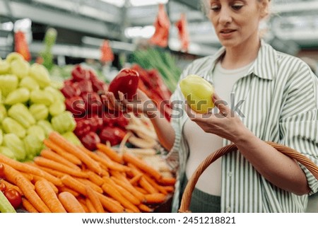 Cropped picture of healthy shopper woman standing near market stall full of vegetables and choosing bell peppers at green market. Selective focus on customer's hands buying produce at food market.