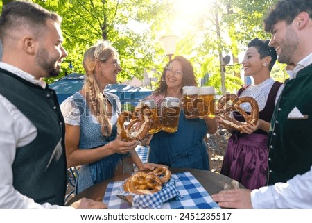 Waitress serving beer to a group of happy friends in traditional tracht at oktoberfest or beer garden in germany Royalty-Free Stock Photo #2451235517