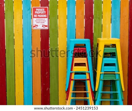 Bright rainbow-colored wooden fence and barstools with a no parking sign.