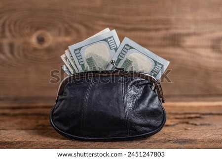 old black genuine leather wallet with banknotes inside on wooden background.
