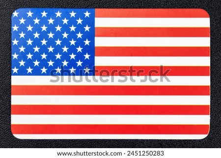 A red, white and blue American flag with stars. The flag is on a black background. The flag is a symbol of the United States of America