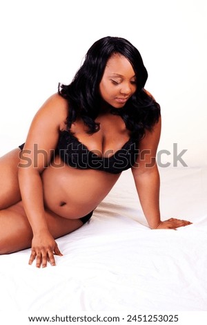 Pregnant African American Woman Sitting On White Sheet In Black Bra And Panties Looking Down