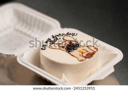 close-up in a white box lies a small white cake with a picture of a dog