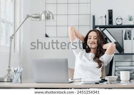 Relaxed professional woman takes a break to stretch at her workstation, signaling a moment of well-deserved rest in her busy day. Royalty-Free Stock Photo #2451254341