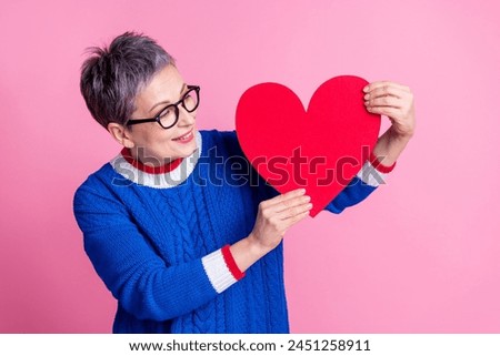 Photo of adorable cute senior woman wear trendy blue clothes look big large red paper card isolated on pink color background