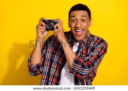 Photo of impressed man with short haircut dressed plaid shirt holding retro camera astonished staring isolated on yellow color background
