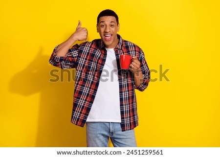 Photo of attractive cheerful man wear trendy checkered clothes showing sign thumb up fresh drink isolated on yellow color background
