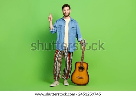 Full length photo of good mood nice guy wear denim jacket playing guitar showing v-sign isolated green color background