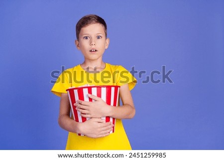 Photo of shocked adorable small boy wear trendy yellow clothes hold popcorn watch horror isolated on purple color background