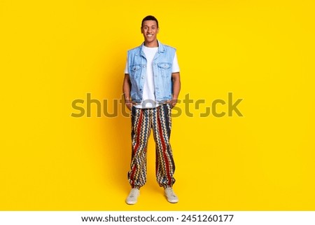 Full length photo of optimistic guy dressed jeans waistcoat pants holding arms in pockets isolated on vibrant yellow color background