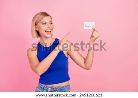 Photo of pretty young woman indicate finger debit card wear blue top isolated on pink color background