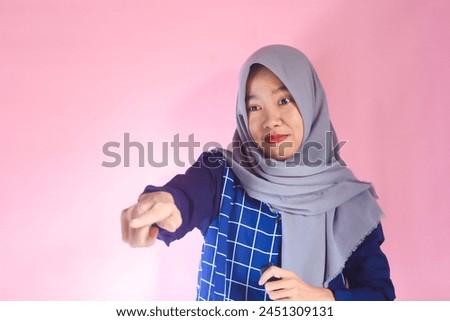 Close up photo of beautiful cheerful Asian Muslim woman, with hand gesture pointing at empty space isolated on pink background