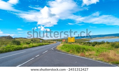 Panoramic over paved Ring road near Egilsstadir in Iceland with beautiful green landscape, lake and blue sky. Information board sign with distances to major cities.